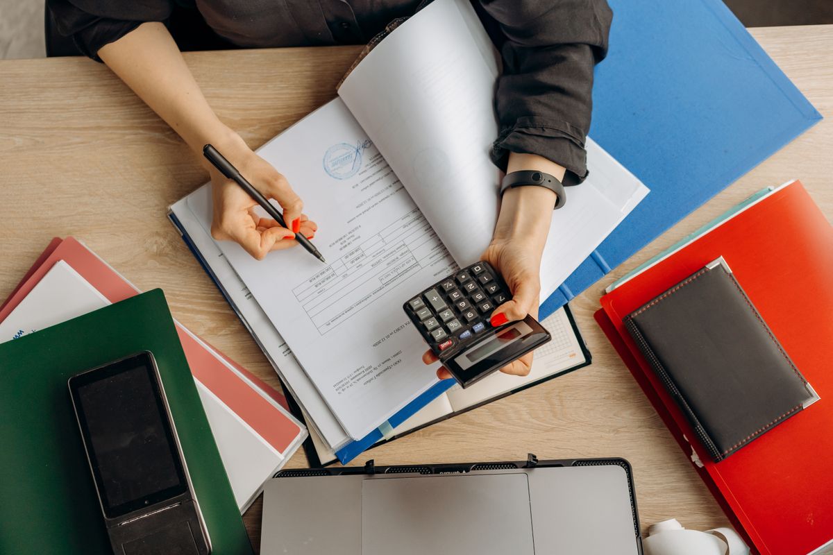 Pessoa conferindo documentos financeiros com calculadora e notebook